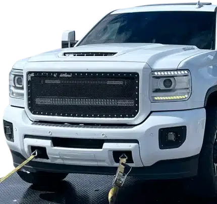 1023 Diesel & Fleet: A white pickup truck with a custom grille and lights, viewed from the front. The truck is secured with yellow tow straps connected to its front.