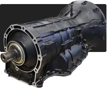 1023 Diesel & Fleet: A close-up image of a black automotive transmission, showcasing its cylindrical structure and detailed metal casing. The component features a visible gear shaft at one end, with intricate details along its surface.