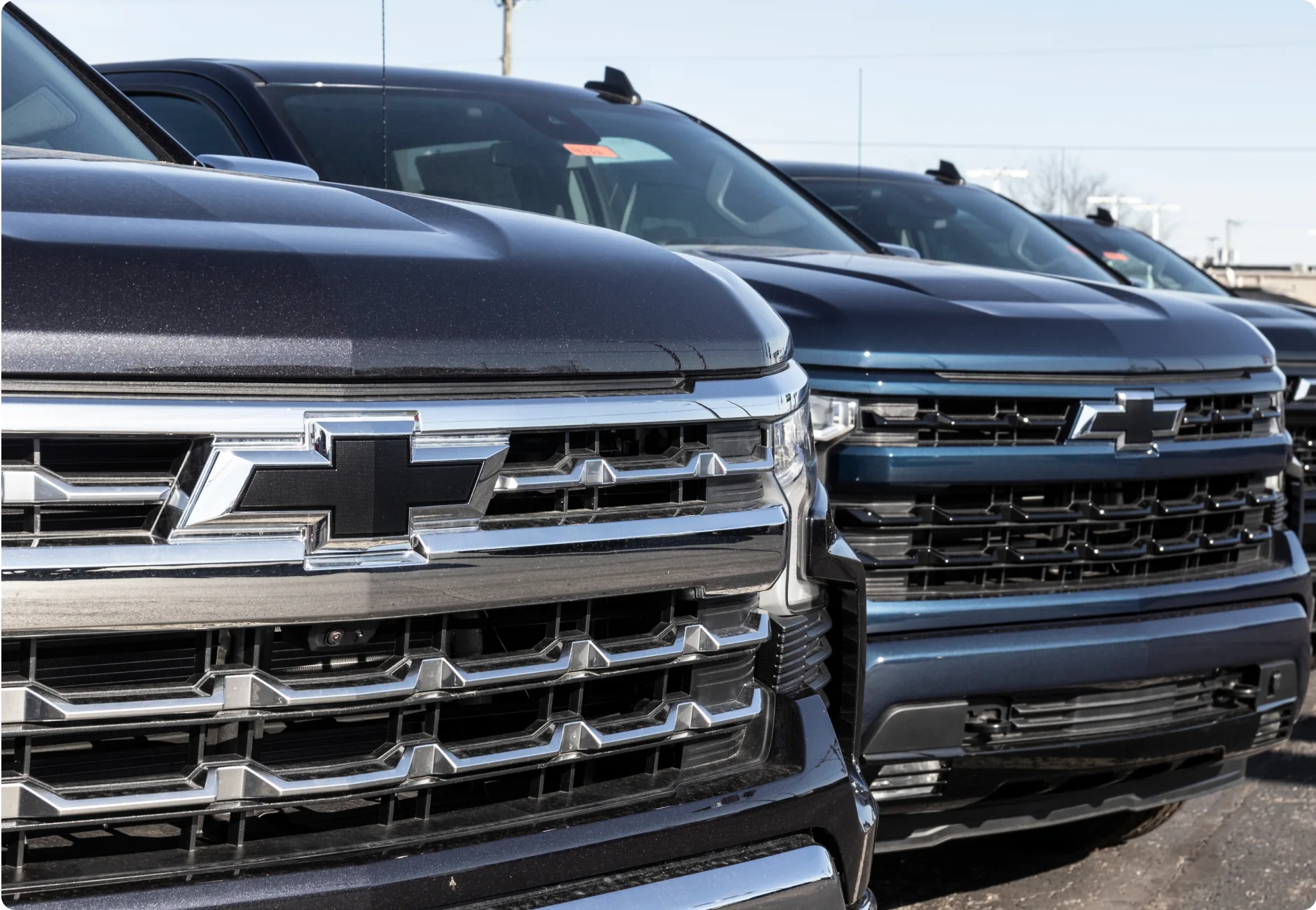 1023 Diesel & Fleet: Close-up of the front grilles of multiple parked Chevrolet trucks, showcasing their shiny chrome details and bold design.