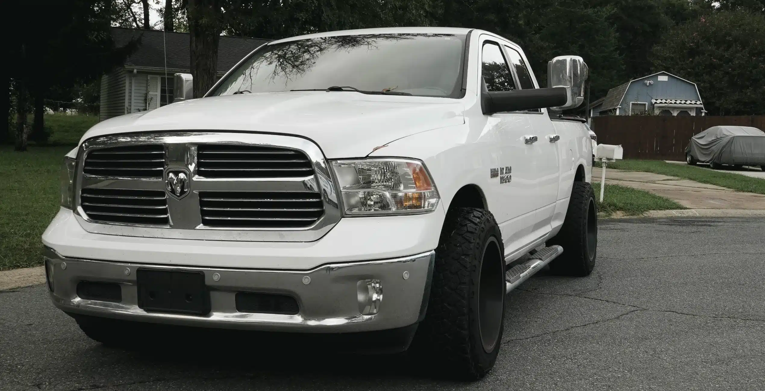 1023 Diesel & Fleet: A white pickup truck with large tires is parked on a residential street. The truck has chrome accents and is positioned at an angle, with houses and greenery visible in the background.