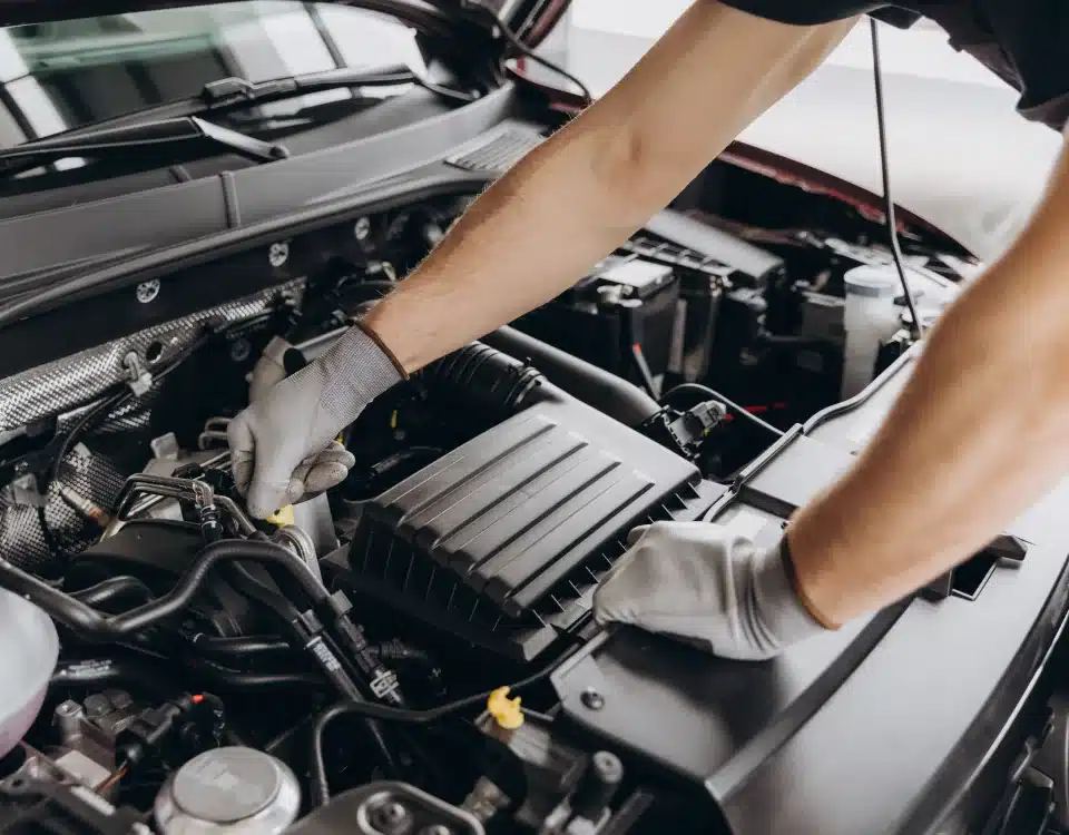 1023 Diesel & Fleet: A mechanic wearing gloves works under the hood of a car, adjusting components of the engine. The focus is on the hands and engine parts.