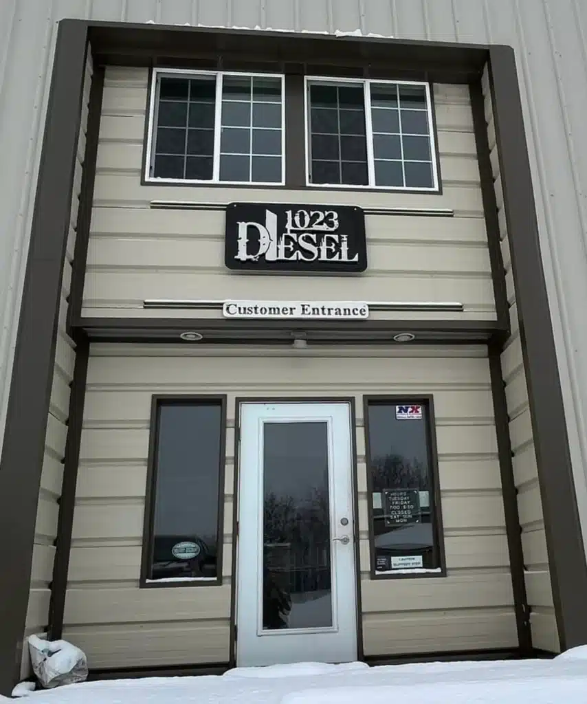 1023 Diesel & Fleet: Entrance to a building with a sign above the door reading 1023 Diesel and Customer Entrance below it. Two large windows are on the second floor, and snow covers the ground outside.