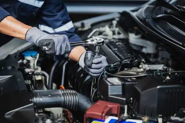 1023 Diesel & Fleet: A mechanic wearing gloves uses a ratchet wrench to work on a car engine, surrounded by various engine components and parts.