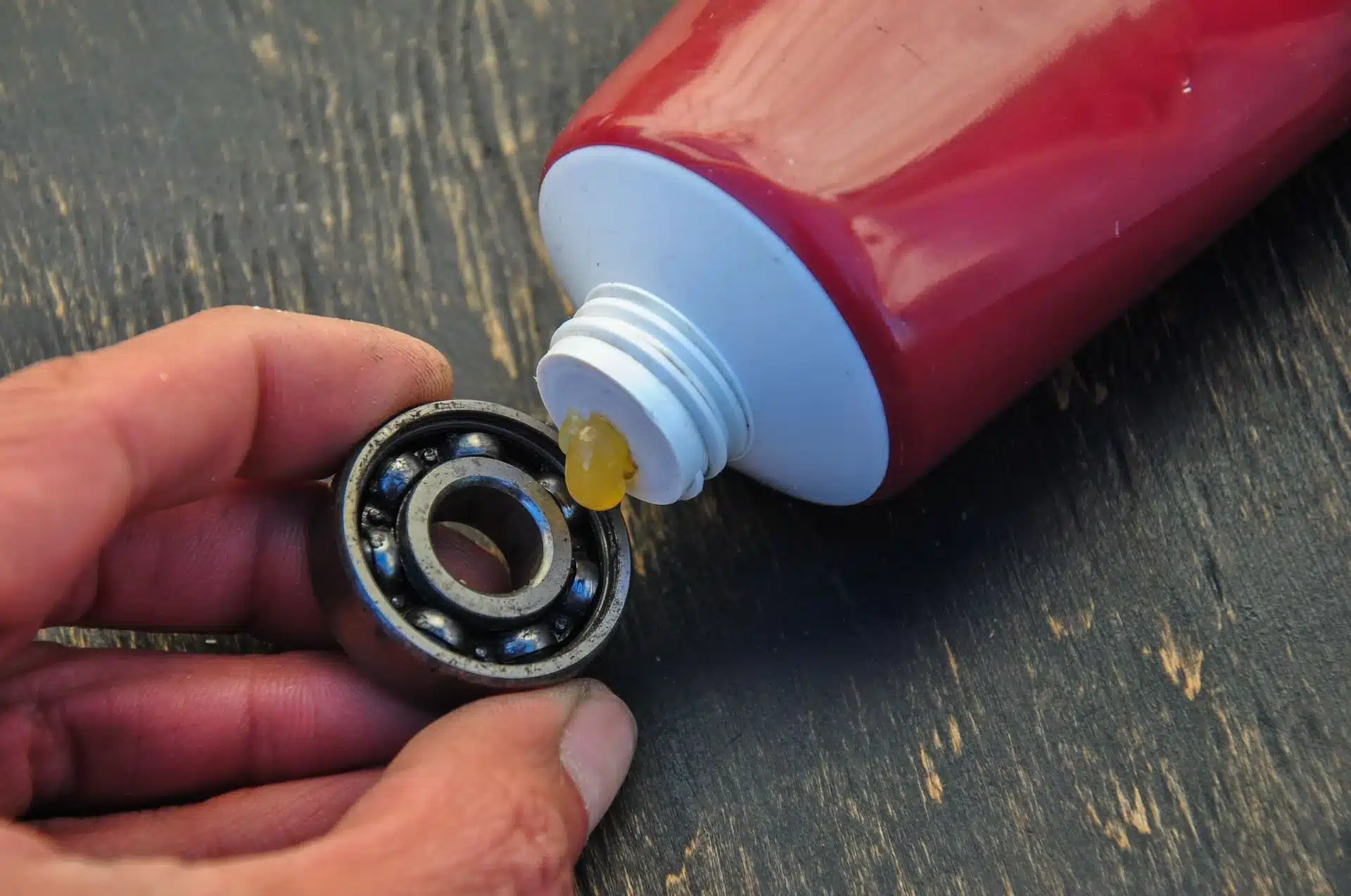 1023 Diesel & Fleet: Hand holding a metal bearing while applying lubricant from a red tube onto it, placed on a wooden surface.