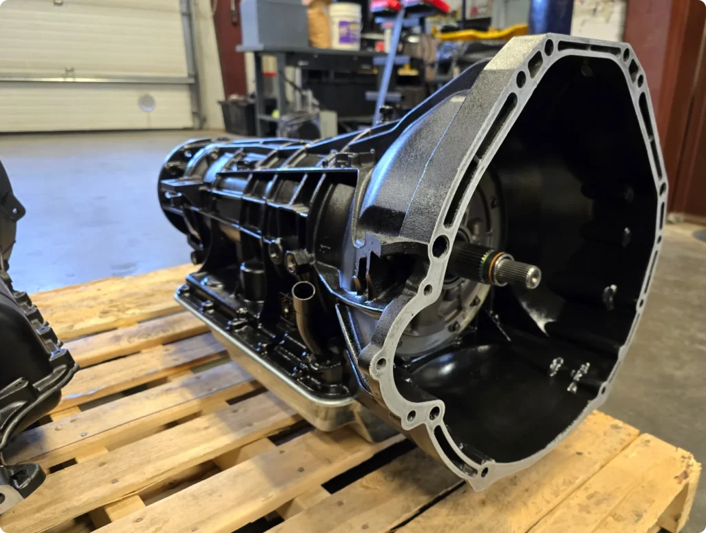 1023 Diesel & Fleet: Close-up of a black, heavy-duty vehicle transmission on a wooden pallet in a workshop setting, with tools and equipment visible in the background.