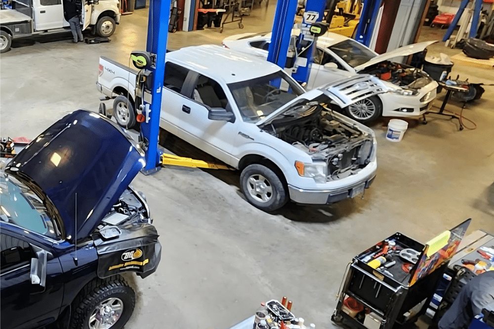 Spring vehicle maintenance, diesel repair in Palmer, AK at 1023 Diesel & Fleet. Overhead view of a busy auto repair shop with multiple vehicles undergoing engine diagnostics and repairs on hydraulic lifts.
