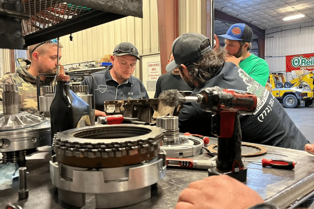 diesel transmission repair, diesel repair in Palmer, AK at 1023 Diesel & Fleet. Technicians gathered around a workbench inside a diesel repair shop, focusing on transmission parts during hands-on training or collaborative repair work.