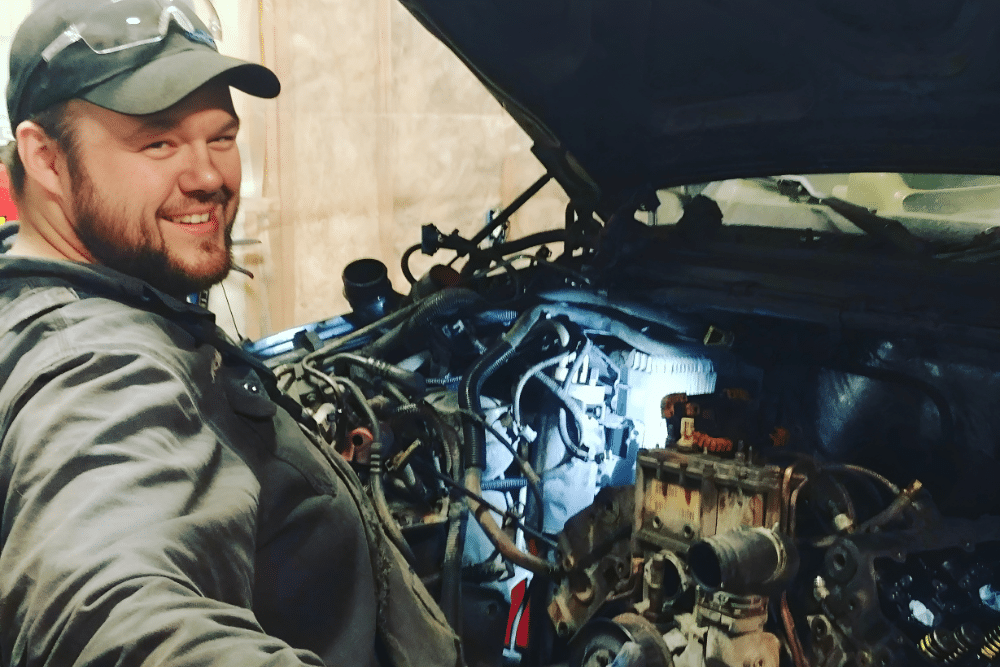 diesel mechanic, diesel repair in Palmer, AK at 1023 Diesel & Fleet. Smiling diesel technician working on a disassembled engine inside a diesel truck, showing hands-on service and in-progress fleet repair in a well-equipped garage.