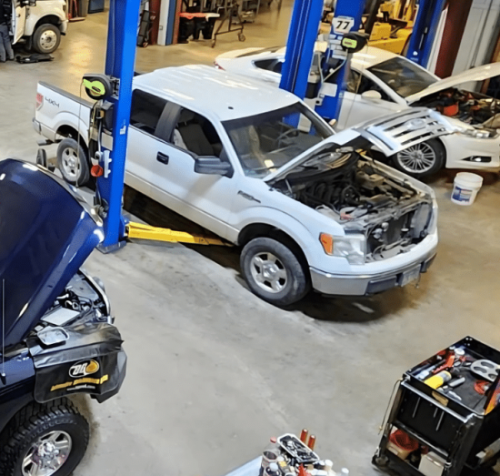 Spring vehicle maintenance, diesel repair in Palmer, AK at 1023 Diesel & Fleet. Overhead view of a busy auto repair shop with multiple vehicles undergoing engine diagnostics and repairs on hydraulic lifts.