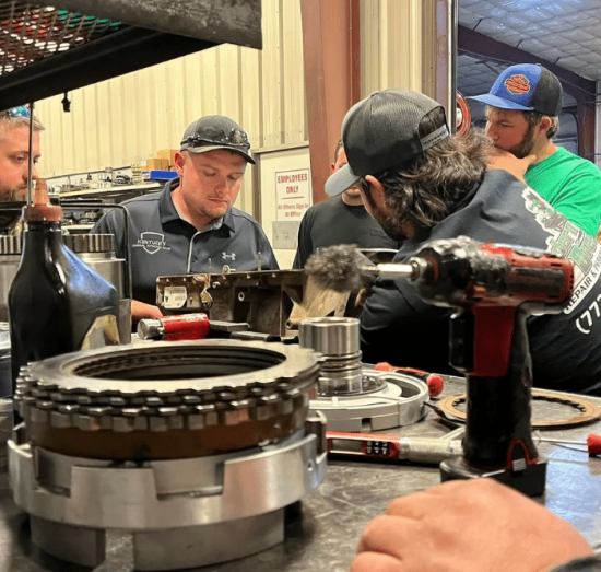 diesel transmission repair, diesel repair in Palmer, AK at 1023 Diesel & Fleet. Technicians gathered around a workbench inside a diesel repair shop, focusing on transmission parts during hands-on training or collaborative repair work.